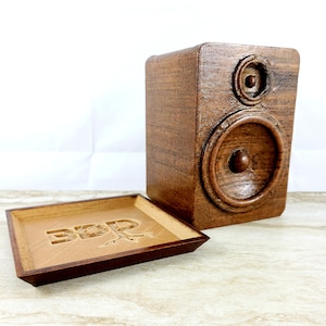 May include: A wooden speaker with a brown wood grain finish. The speaker has a large round speaker cone and a smaller round tweeter. The speaker is sitting on a wooden tray with the word "3DP" carved into it.