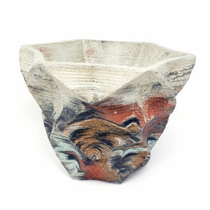 May include: A white ceramic planter with a geometric shape and a multi-colored glaze. The glaze features shades of blue, red, brown, and gold.