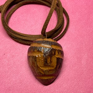 May include: A brown wooden heart-shaped pendant with intricate carvings, hanging from a brown leather cord.