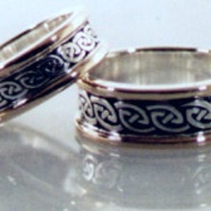 May include: Two silver wedding bands with a Celtic knot design. The bands are wide and have a polished finish.