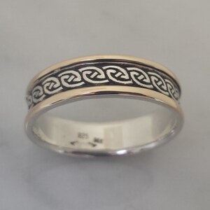 May include: Silver ring with a gold band and a black Celtic knot design. The ring has a polished finish and a classic, timeless style. The intricate knotwork adds a touch of elegance.