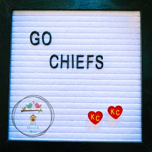 May include: A white letter board with the words "GO CHIEFS" in black letters. There are two red hearts with the letters "KC" in yellow on the board. The bottom of the board has a small logo with a birdhouse and the words "2311 Decor & More".