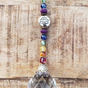 Peut inclure: Une boule de cristal transparente avec un sommet en métal argenté pend à une chaîne de perles colorées. Les perles sont dans les couleurs de l'arc-en-ciel et comprennent un charme argenté avec un motif de fleur de lotus.