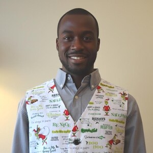 May include: A white vest featuring a repeating pattern of green Grinch characters and various holiday-themed phrases such as Be Nice, Naughty, and It Wouldn't Be Christmas Without Me, secured with three black buttons over a grey collared shirt.