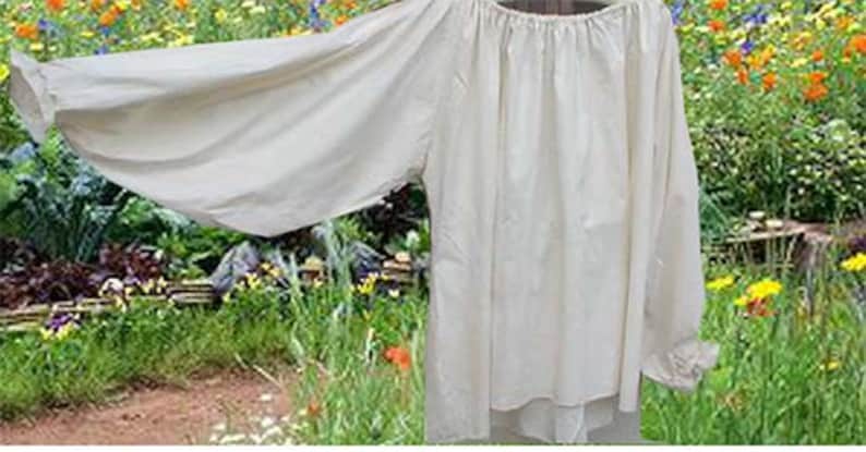 Pode incluir: Uma camisa branca de manga comprida com gola franzida. A camisa &eacute; feita de um tecido leve e tem um caimento solto. Est&aacute; pendurada em um varal em um jardim.