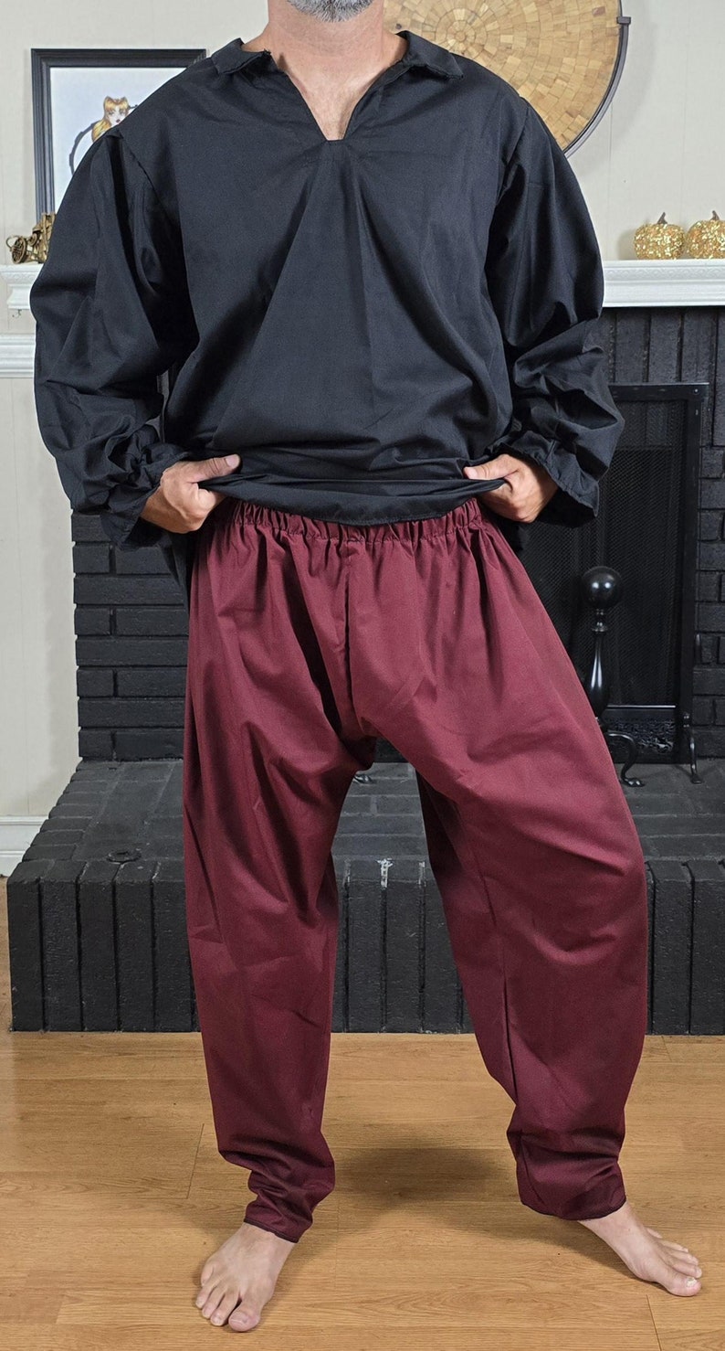 Puede incluir: Una persona vistiendo una camisa negra de manga larga con cuello en V y pantalones marrones.