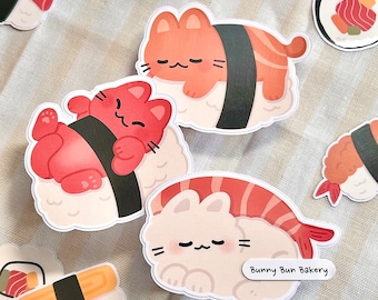 May include: A collection of cute sushi cat stickers. The stickers feature various cat designs on top of sushi, including salmon, shrimp, and tamago. The stickers are white with a light beige background and the text "Bunny Bun Bakery".