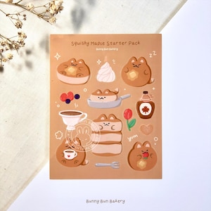 May include: A sheet of stickers featuring cartoon illustrations of a brown bunny with maple syrup, pancakes, whipped cream, and other breakfast foods. The text "Squishy Maple Starter Pack" and "Bunny Bun Bakery" is printed on the sheet.