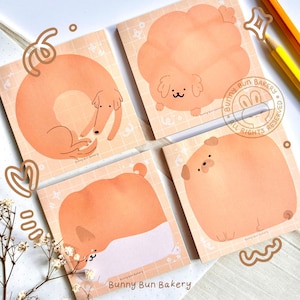 May include: Four square notepads with illustrations of cartoon dogs in various poses. The notepads are peach-colored with a grid pattern and the text "Bunny Bun Bakery".