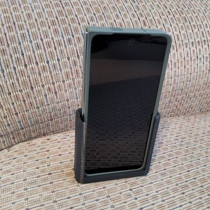 May include: A black phone case with a green phone inside. The phone is in a vertical position and is sitting on a brown couch.