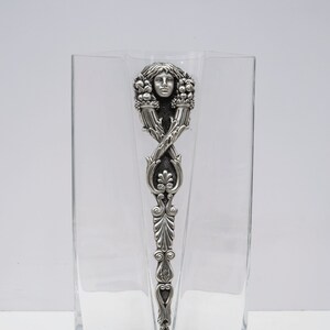 May include: A clear glass vase with a silver-toned metal design featuring a woman's face and floral motifs.