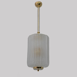 May include: A clear glass pendant light with a ribbed cylindrical shade. The light fixture has gold-colored metal accents at the top and bottom, and a twisted rope-like cord. The light hangs from a gold-colored ceiling mount.