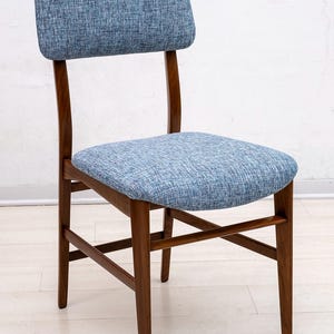May include: A mid-century modern chair with a blue upholstered seat and backrest. The chair has a wooden frame with a dark brown finish. The chair's design features curved back legs and a rectangular backrest.