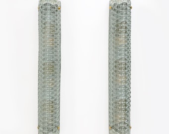 May include: Two vintage, textured glass wall sconces. Each sconce is a long, cylindrical shape with a repeating diamond pattern. The glass has a pale green hue, and each sconce has small gold-coloured accents at the top and bottom.