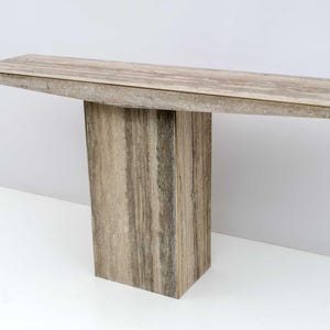 Puede incluir: Una consola rectangular con una tapa texturizada de color marrón claro y una base maciza a juego. La mesa está hecha de un material similar a la piedra y mide aproximadamente 152 cm de largo.