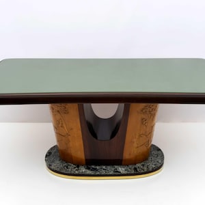 May include: A rectangular table with a light green top and dark brown trim. The base is made of light and dark wood with carved floral designs. The table sits on a gray and gold base.
