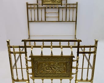 May include: A vintage brass bed frame with ornate detailing. The headboard features a rectangular relief with a religious scene, and the footboard has a similar design. The frame includes twisted vertical bars and decorative horizontal elements.