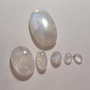 May include: Six oval-shaped moonstone cabochons in various sizes, ranging from small to large. The stones are a milky white color with a slight iridescent sheen.