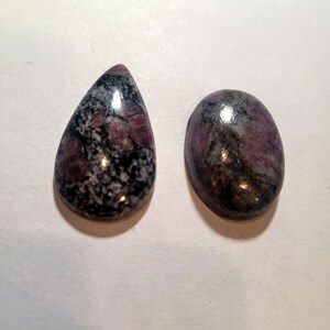 May include: Two cabochon gemstones, one teardrop shaped and one oval, with a black and white speckled pattern and pink accents.