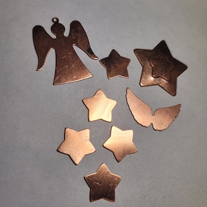 May include: A collection of copper-colored metal charms in the shape of stars and angels. The charms are perfect for jewelry making or crafting.