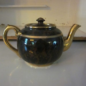 May include: A black teapot with gold trim and a brown and black patterned design.