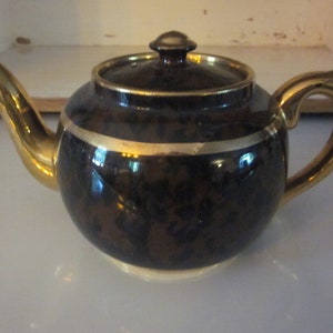 May include: A brown teapot with a gold trim and a gold handle. The teapot has a mottled brown glaze.