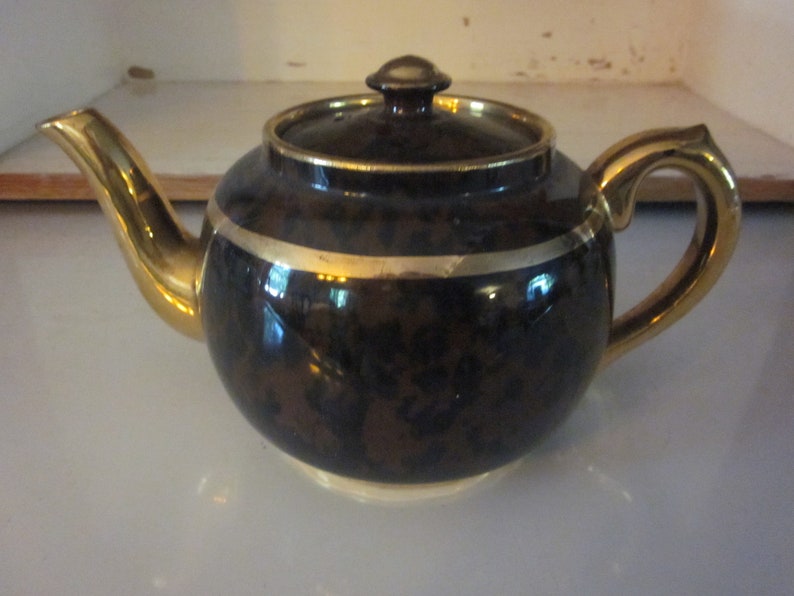 May include: A brown teapot with a gold trim and a gold handle. The teapot has a mottled brown glaze.