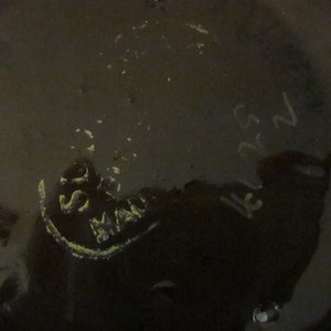 May include: Close-up of the bottom of a dark brown ceramic vase with a white stamp that reads "550 Made in Japan" and a handwritten inscription that reads "152".