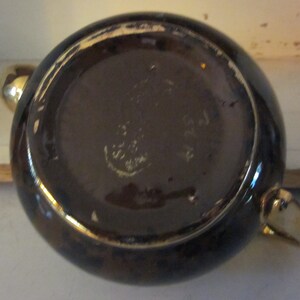 May include: The bottom of a brown teapot with gold trim. The teapot has a maker's mark that reads "Made in England".