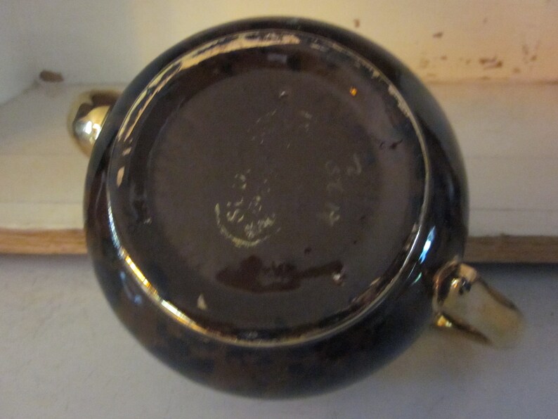 May include: The bottom of a brown teapot with gold trim. The teapot has a maker's mark that reads "Made in England".