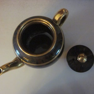 May include: A black teapot with gold trim and a matching lid. The teapot has a round body and a spout. The lid has a small knob on top.