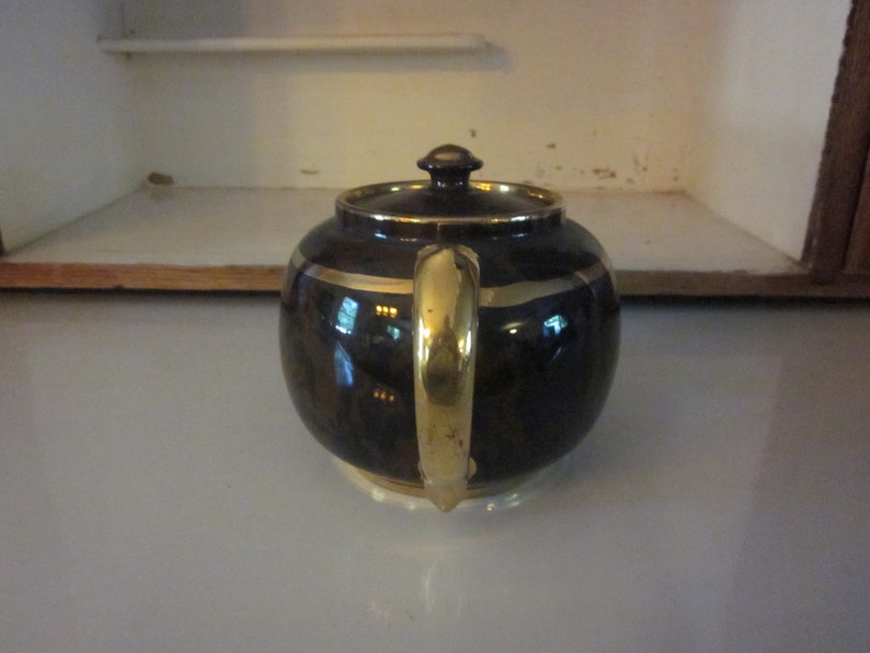 May include: A brown teapot with a gold handle and trim. The teapot has a round body and a lid with a knob on top.