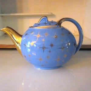 May include: A blue teapot with a gold star pattern. The teapot has a gold handle and spout.