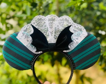 May include: Green and black striped fabric mouse ears with a white lace trim and a black velvet bow with bat wings.