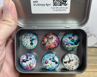 May include: A set of six round magnets with hummingbird designs in a silver tin. Each magnet features a different hummingbird illustration with colourful floral backgrounds. The tin includes a label that says "Thank you for shopping with It's Simply Ryn!"