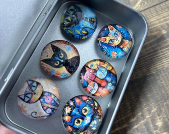 May include: Six decorative cat magnets in a silver tin. Each round magnet showcases a colourful cat design with floral and abstract patterns. The cats are depicted in various colours, including blue, orange, and black.