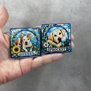 May include: Two square decorative tiles featuring stained glass style illustrations of dogs. One tile shows a white and brown dog with a sunflower and the name DIESEL. The other tile shows a yellow dog with white flowers and the name SPROCKET.