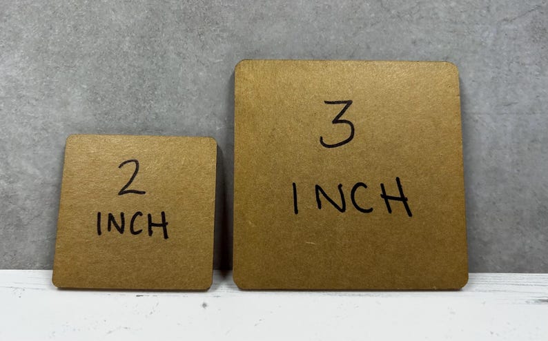 May include: Two square brown cardboard pieces with rounded corners. The smaller piece has the text 2 INCH written in black marker, and the larger piece has the text 3 INCH written in black marker, indicating their respective sizes in inches.