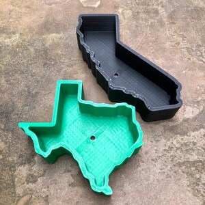 May include: A black 3D-printed container shaped like the state of California and a green 3D-printed container shaped like the state of Texas. Both containers feature high walls, a hollow interior, and a single circular drainage hole at the base.