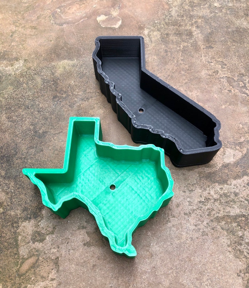 May include: A black 3D-printed container shaped like the state of California and a green 3D-printed container shaped like the state of Texas. Both containers feature high walls, a hollow interior, and a single circular drainage hole at the base.