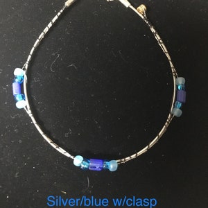 May include: A silver and blue beaded anklet with a clasp. The anklet is made of silver wire and has blue glass beads.