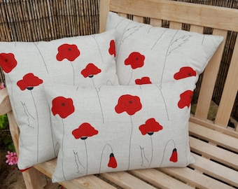 May include: Four throw pillows with a white linen fabric and a red poppy flower pattern. The pillows are arranged on a wooden bench.