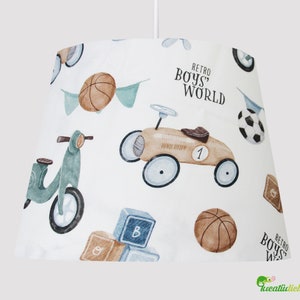 Peut inclure: Abat-jour blanc sur le thème du monde rétro des garçons. Le motif présente un scooter bleu, une voiture jouet jaune, des ballons de basket, des blocs de construction et un ballon de football. Le texte "Retro Boys' World" est imprimé sur l'abat-jour.