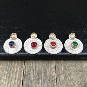 Puede incluir: Cuatro colgantes de plata con piedras de vidrio de diferentes colores. Los colgantes son redondos y tienen un dise&ntilde;o decorativo. Las piedras son azules, rojas, verdes y transparentes.