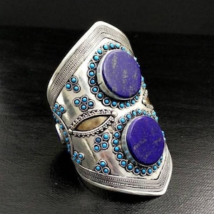 Può includere: Un braccialetto rigido in argento con un designo decorativo che presenta due grandi pietre di lapislazzuli e pietre turchesi più piccole.