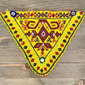 May include: A yellow triangular beaded piece with a geometric pattern in red, blue, and green. The piece is made of small beads and has a fringe border.