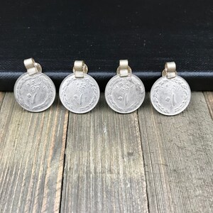 Puede incluir: Cuatro colgantes de moneda de color plateado con un lazo dorado en la parte superior. Las monedas tienen un dise&ntilde;o de un &aacute;rbol con un p&aacute;jaro en una rama.