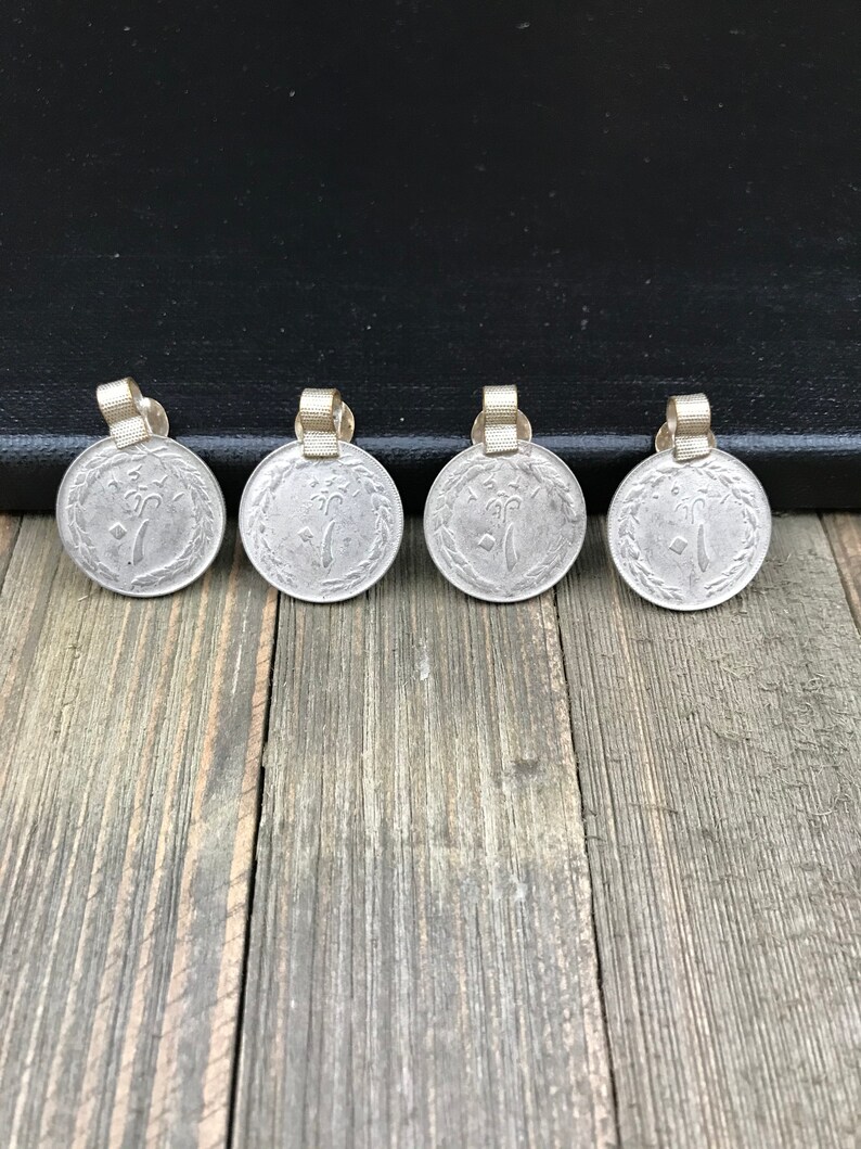 Puede incluir: Cuatro colgantes de moneda de color plateado con un lazo dorado en la parte superior. Las monedas tienen un dise&ntilde;o de un &aacute;rbol con un p&aacute;jaro en una rama.