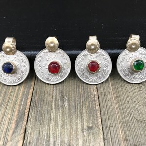 Puede incluir: Cuatro colgantes de moneda de plata con piedras de vidrio de diferentes colores en el centro. Las piedras son azules, rojas, rojas y verdes.