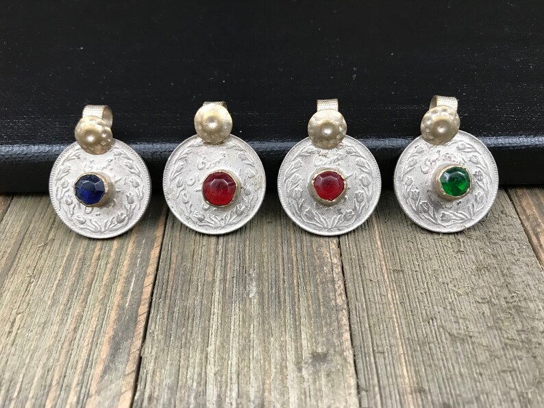 Puede incluir: Cuatro colgantes de moneda de plata con piedras de vidrio de diferentes colores en el centro. Las piedras son azules, rojas, rojas y verdes.
